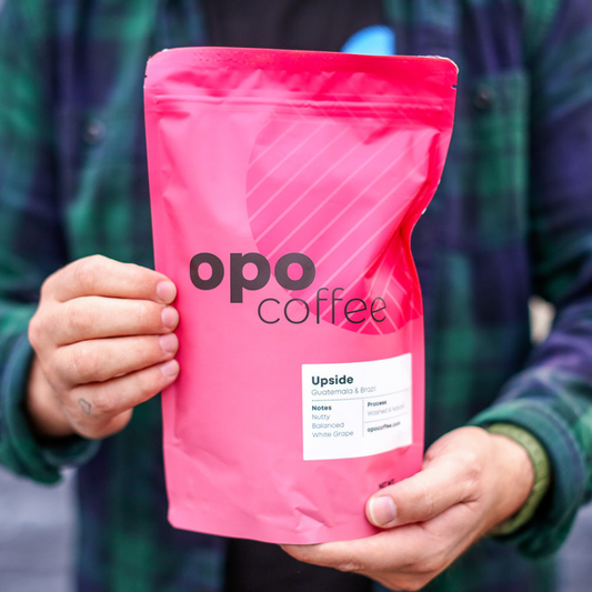 Hands holding pink coffee bag in front of plaid shirt