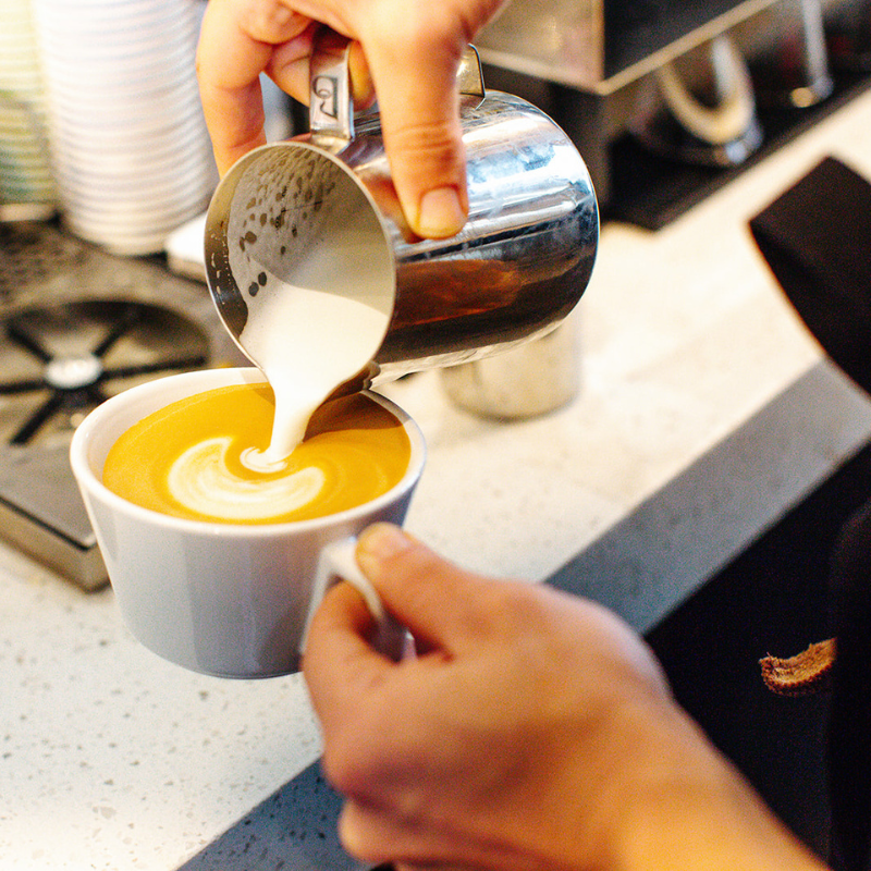 Hand pouring milk into a white mug