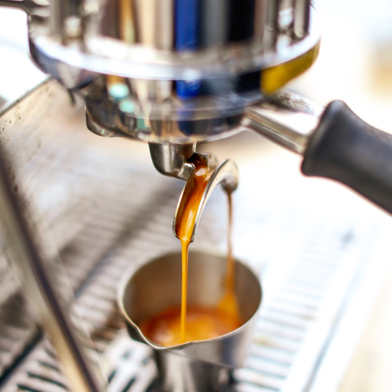 Espresso shot pouring from portafilter, into metal cup